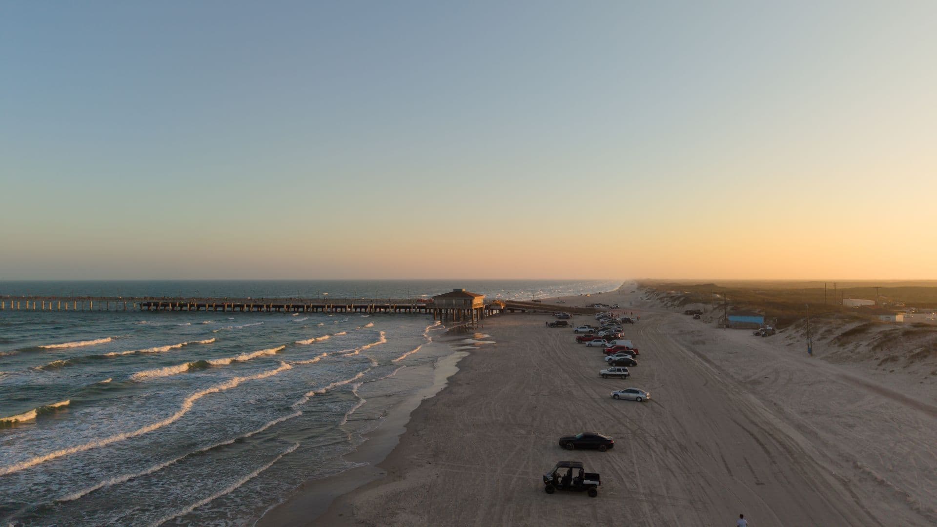 Fishing pier and beach at sunset with trucks parked on the sand