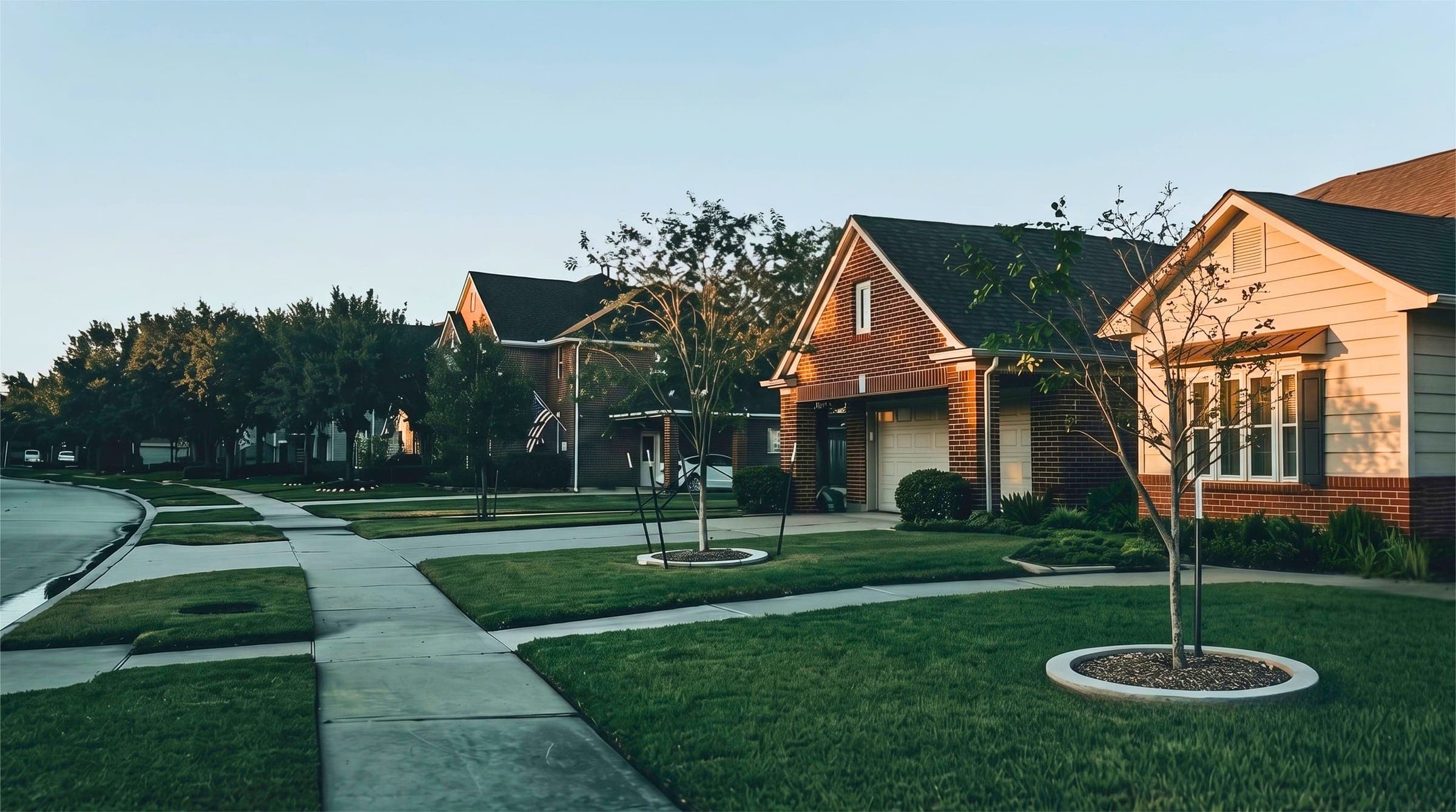 Suburban street of brick homes with young trees and sidewalks at dusk