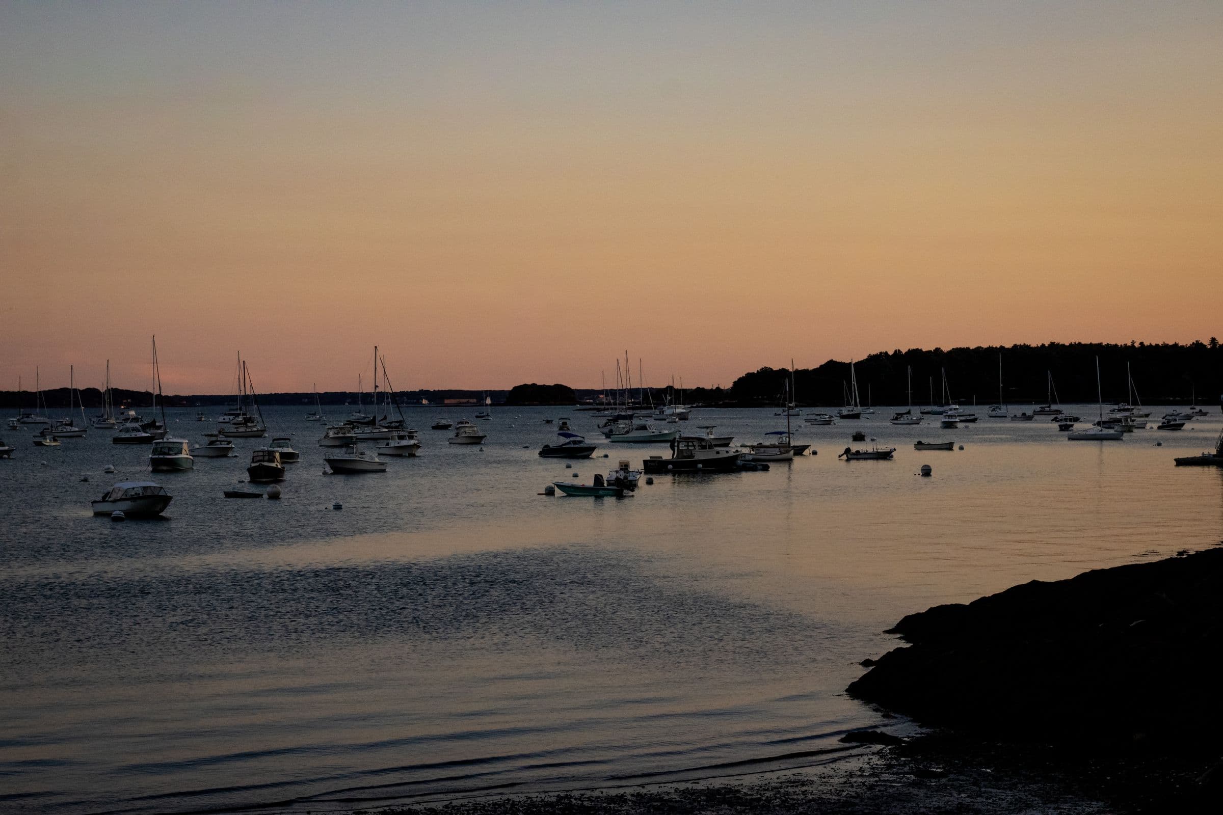 Boats moored along a calm bay shoreline under a warm sunset horizon